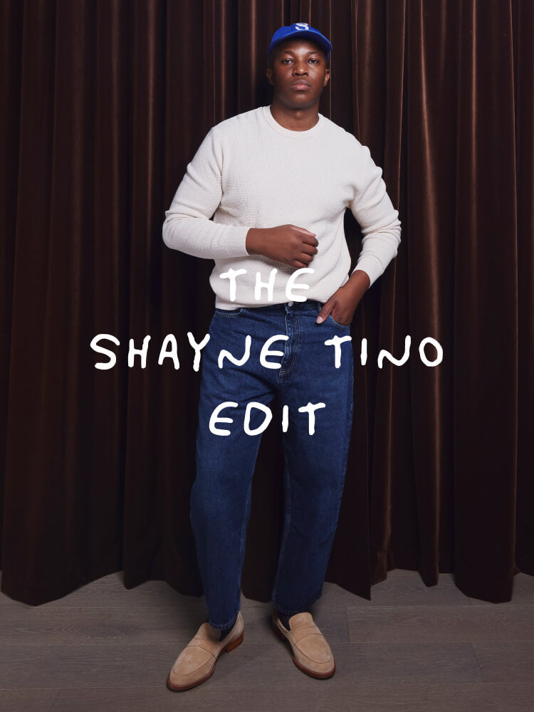 Man wearing a white sweater and blue jeans with text 'The Shayne Tino Edit' against a brown curtain background.