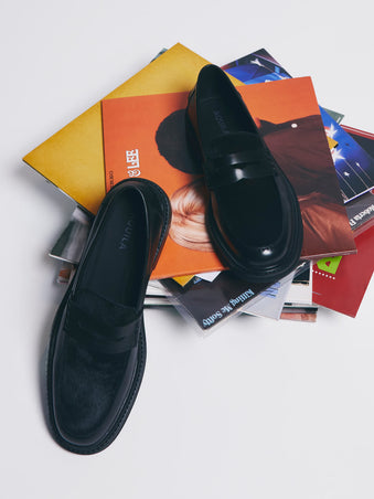 Black loafers on a stack of magazines with a white background