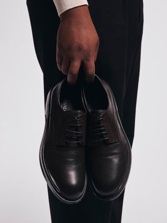 Person holding a pair of black leather shoes against a white background