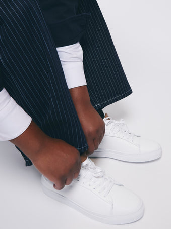 Person wearing a dark pinstripe suit and white sneakers on a light background